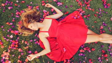 Beautiful Young Woman Lying on Grass with Flowers In Red Dress
